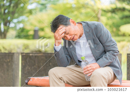 Elderly man sitting on a park bench (headache) 103021617