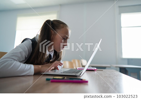 Caucasian girl sits at a desk at school and carefully looks into a laptop. Caucasian girl sits at a desk at school and carefully looks into a laptop. 103022523