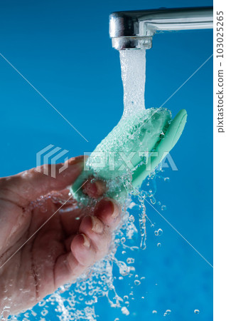 A woman washes a vibrator under running water on a blue background. Women's Health Kegel Trainer.  103025265