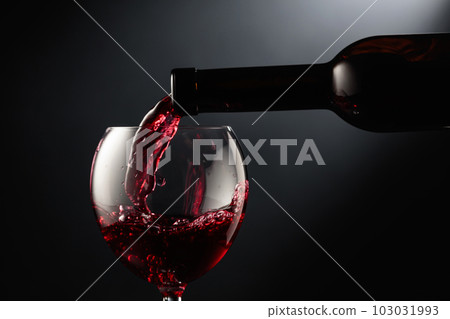Pouring red wine into a wine glass. Pouring red wine into a wine glass. 103031993