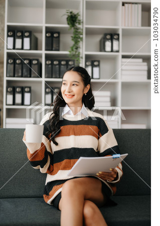 Beautiful asian woman holding and using digital tablet while drinking coffee at home office and cafe Beautiful asian woman holding and using digital tablet while drinking coffee at home office and cafe 103034790