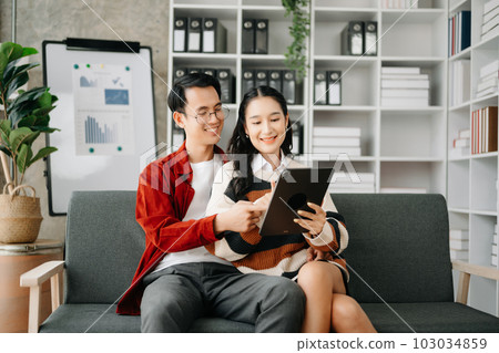 Two asian students learning together online with a laptop, tablet and tutor together in liveing room at home.. 103034859