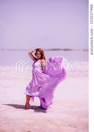 Woman pink salt lake. Against the backdrop of a pink salt lake, a woman in a long pink dress takes a leisurely stroll along the white, salty shore, capturing a wanderlust moment. 103037466