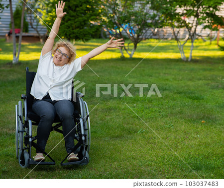 Elderly caucasian woman doing exercises while sitting in a wheelchair outdoors. Elderly caucasian woman doing exercises while sitting in a wheelchair outdoors. 103037483