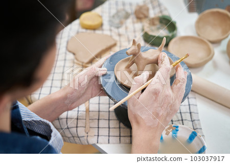 woman sculpts a figurine of a dog from clay by hands, closeup in artistic studio woman sculpts a figurine of a dog from clay by hands, closeup in artistic studio 103037917
