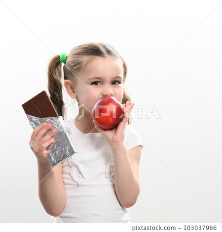 Little cute girl chooses apple over chocolate, preference of healthy food over unhealthy and unhealthy. 103037966