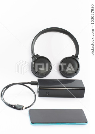 Wireless bluetooth headphones on white background with power bank and charging cable and phone. Wireless bluetooth headphones on white background with power bank and charging cable and phone. 103037980