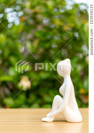 Ceramic Yoga Figurine of Woman doing yoga pose on wooden floor and green leaf background Ceramic Yoga Figurine of Woman doing yoga pose on wooden floor and green leaf background 103038135