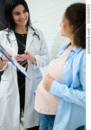 Confident experienced doctor gynecologist obstetrician holding clipboard with analyses and ultrasound scan results, explaining to pregnant woman the treatment that needs to perform in obstetric clinic Confident experienced doctor gynecologist obstetrician holding clipboard with analyses and ultrasound scan results, explaining to pregnant woman the treatment that needs to perform in obstetric clinic 103040953
