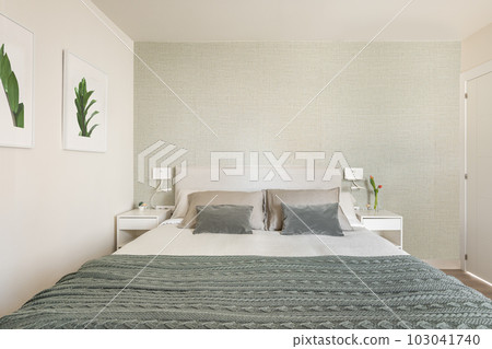 Stylish bright bedroom with bedside tables and a double bed with green beige wallpaper and cute pictures on the wall. The concept of a small but cozy and multifunctional apartment. Copyspace 103041740
