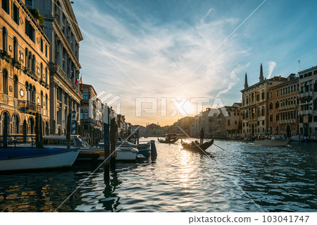 Gondolier on a gondola floats along a canal in Venice in the middle of ancient buildings on an early sunny morning. Beautiful romantic travel concept. Copyspac 103041747