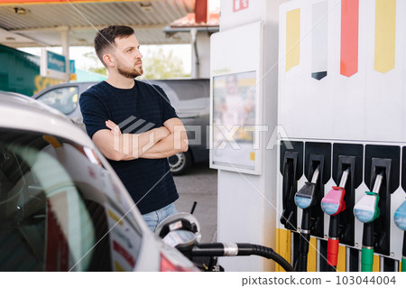 Handsome bearded man cross the arms during refueling car. Male looking on the scoreboard while standing on self service gas station 103044004