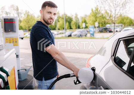 Handsome man refuelling his car on self service gas station. Male filling diesel at gasoline fuel in car using a fuel nozzle. Petrol concept. 103044012