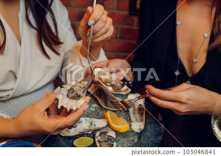Flat lay of caucasian hands holding oysters with other seafood dishes on a dark table. Flat lay of caucasian hands holding oysters with other seafood dishes on a dark table. 103046841