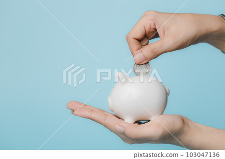 Hand saving a coin into piggy bank  on blue background 103047136