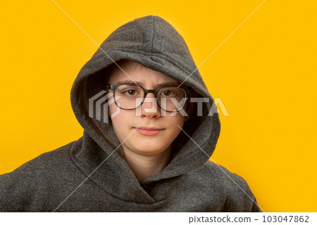 Portrait of boy with glasses wears hoodie and hood on yellow background. Shy unsociable teenager. Portrait of boy with glasses wears hoodie and hood on yellow background. Shy unsociable teenager. 103047862