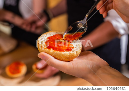 Chef smears a bun with ketchup for hamburger close up - food and cooking concept Chef smears a bun with ketchup for hamburger close up - food and cooking concept 103049681