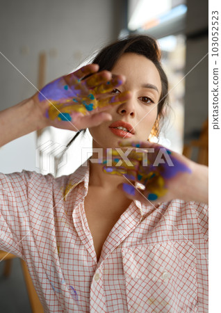 Creative portrait of young artist looking at camera through painted hands Creative portrait of young artist looking at camera through painted hands 103052523