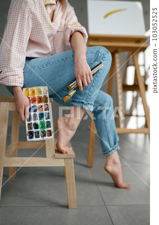 Cropped shot of barefoot female artist holding drawing tools sitting on chair 103052525