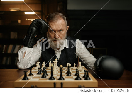 Serious senior man chess player sitting at chessboard Serious senior man chess player sitting at chessboard 103052626