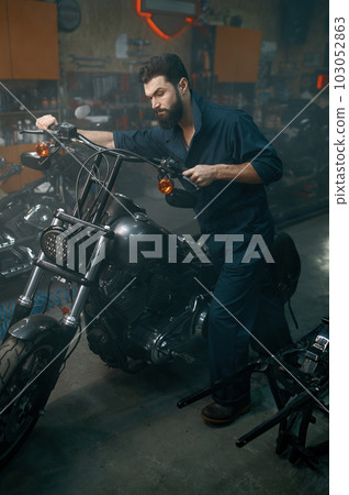Auto mechanic pushing motorcycle on repair stand in workshop garage Auto mechanic pushing motorcycle on repair stand in workshop garage 103052863