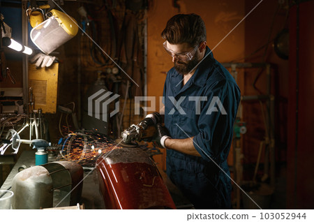 Repairman grinding motorcycle body part from old paint using stripping machine Repairman grinding motorcycle body part from old paint using stripping machine 103052944