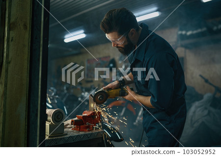 Repairman cutting iron with electric circular saw in motorcycle workshop 103052952