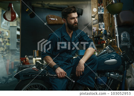 Portrait of confident man in overalls holding wrench while sitting on motorcycle 103052953
