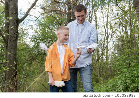 Dad showing paper plane to happy son outdoors, spending time together Dad showing paper plane to happy son outdoors, spending time together 103052982