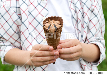 Child's hands holding chocolate brown ice cream in a waffle cone outdoors in summer Child's hands holding chocolate brown ice cream in a waffle cone outdoors in summer 103053000