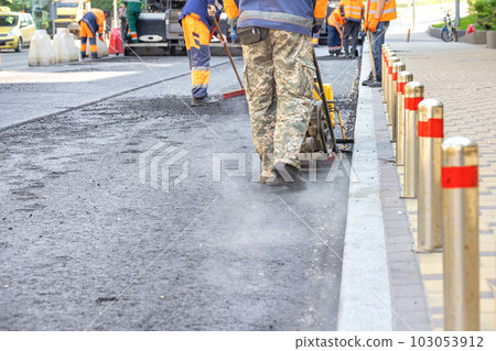 A team of road service workers lays fresh asphalt at a road construction site. 103053912