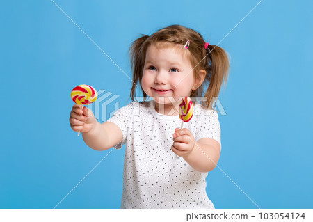 Beautiful little female child holding huge lollipop spiral candy smiling happy isolated on blue background. Beautiful little female child holding huge lollipop spiral candy smiling happy isolated on blue background. 103054124