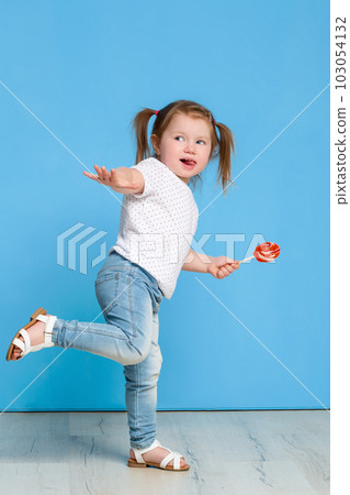 Beautiful little female child holding huge lollipop spiral candy smiling happy isolated on blue background. Beautiful little female child holding huge lollipop spiral candy smiling happy isolated on blue background. 103054132