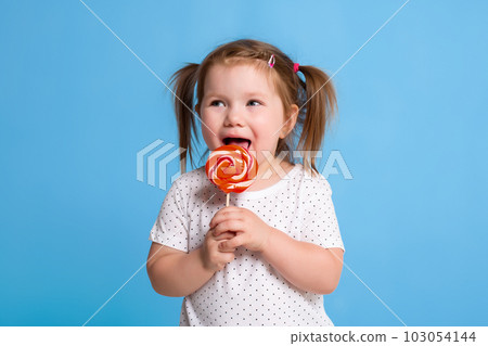Beautiful little female child holding huge lollipop spiral candy smiling happy isolated on blue background. Beautiful little female child holding huge lollipop spiral candy smiling happy isolated on blue background. 103054144