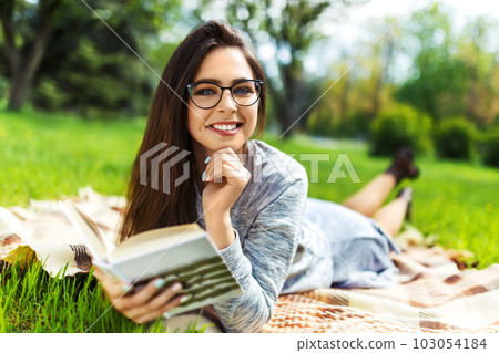 Beautiful relaxed woman readingbook at lawn with sun shining. Girl gets pleasure from reading book. Beautiful relaxed woman readingbook at lawn with sun shining. Girl gets pleasure from reading book. 103054184