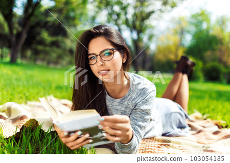 Beautiful relaxed woman readingbook at lawn with sun shining. Girl gets pleasure from reading book. Beautiful relaxed woman readingbook at lawn with sun shining. Girl gets pleasure from reading book. 103054185