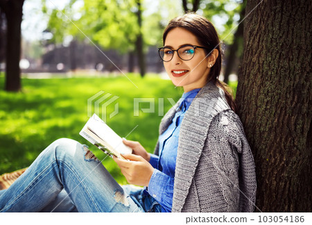 Beautiful relaxed woman readingbook at lawn with sun shining. Girl gets pleasure from reading book. Beautiful relaxed woman readingbook at lawn with sun shining. Girl gets pleasure from reading book. 103054186