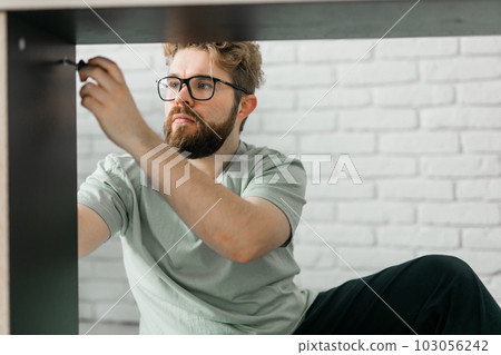 Young attractive man assembles furniture - handwerker and interior objects concept 103056242