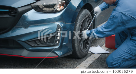 Close up of Young mechanic cropped hand of fixing tire with wearing blue uniform. Car mechanic squatting next to the car in the auto repair shop. Mature man holding changing car wheel. 103056279