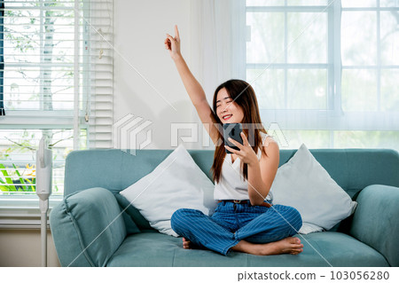 Lifestyle woman wireless earphone chill a little dancing from music application smartphone, Asian young female wear earbuds listening to music on sofa with smart mobile phone in living room at home Lifestyle woman wireless earphone chill a little dancing from music application smartphone, Asian young female wear earbuds listening to music on sofa with smart mobile phone in living room at home 103056280
