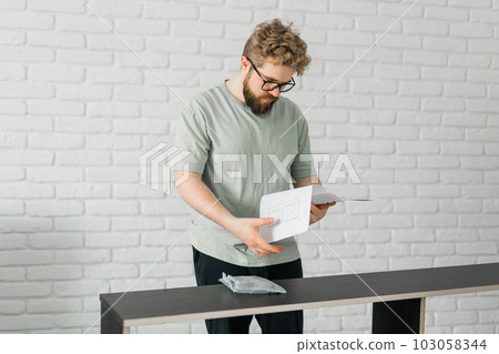 Bearded millennial man assemble his bookcase. He uses tools for furniture. Furniture for the interior room or apartments Bearded millennial man assemble his bookcase. He uses tools for furniture. Furniture for the interior room or apartments 103058344