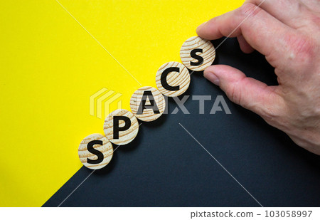 SPACs symbol. Wooden circles with words 'SPACs, special purpose acquisition companies' on beautiful black and yellow background, copy space. Businessman hand. Business and SPACs concept. 103058997