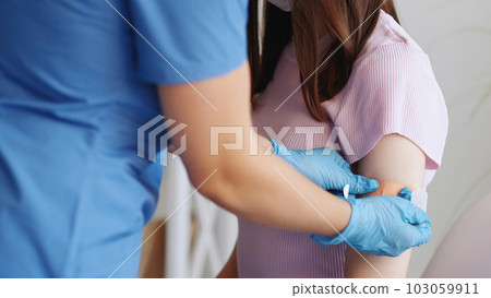 Vaccination process. Covid-19 prevention. Unrecognizable doctor hand in gloves pasting plaster after injection to female patient arm shoulder in clinic. 103059911