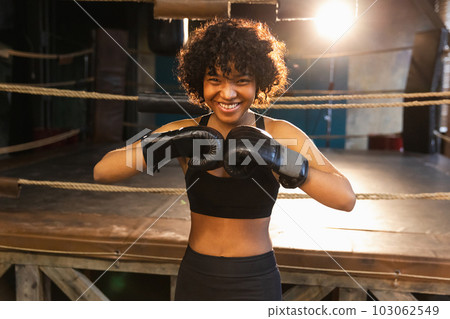 Outcry independent girl power. Angry african american woman fighter with boxing gloves looking serious aggressive standing on boxing ring. Strong powerful fighter girl training punches 103062549
