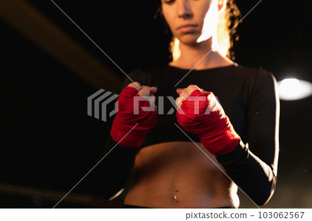 Women self defense girl power. Woman fighter preparing for fight wrapping hands with red boxing wraps sports protective bandages. Strong hands ready for fight active exercise sparring workout training Women self defense girl power. Woman fighter preparing for fight wrapping hands with red boxing wraps sports protective bandages. Strong hands ready for fight active exercise sparring workout training 103062567