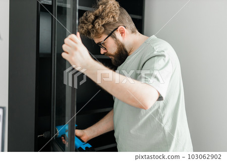 Young attractive man assembles furniture - handwerker and interior objects concept Young attractive man assembles furniture - handwerker and interior objects concept 103062902