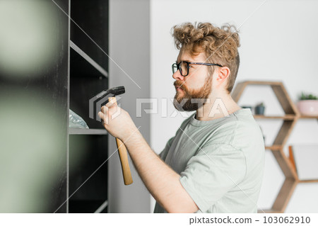 Young attractive man assembles furniture - handwerker and interior objects concept Young attractive man assembles furniture - handwerker and interior objects concept 103062910