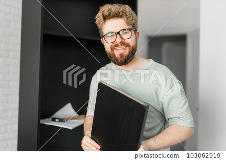 Young attractive man assembles furniture - handwerker and interior objects concept Young attractive man assembles furniture - handwerker and interior objects concept 103062919