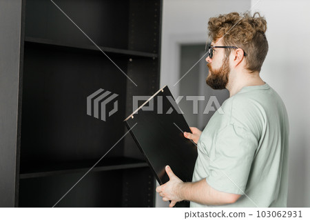 Young attractive man assembles furniture - handwerker and interior objects concept Young attractive man assembles furniture - handwerker and interior objects concept 103062931