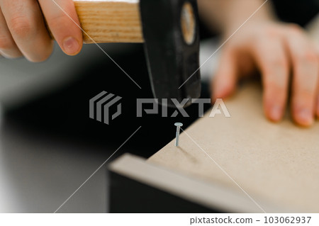 Close up of hammering a nail into wooden board Close up of hammering a nail into wooden board 103062937
